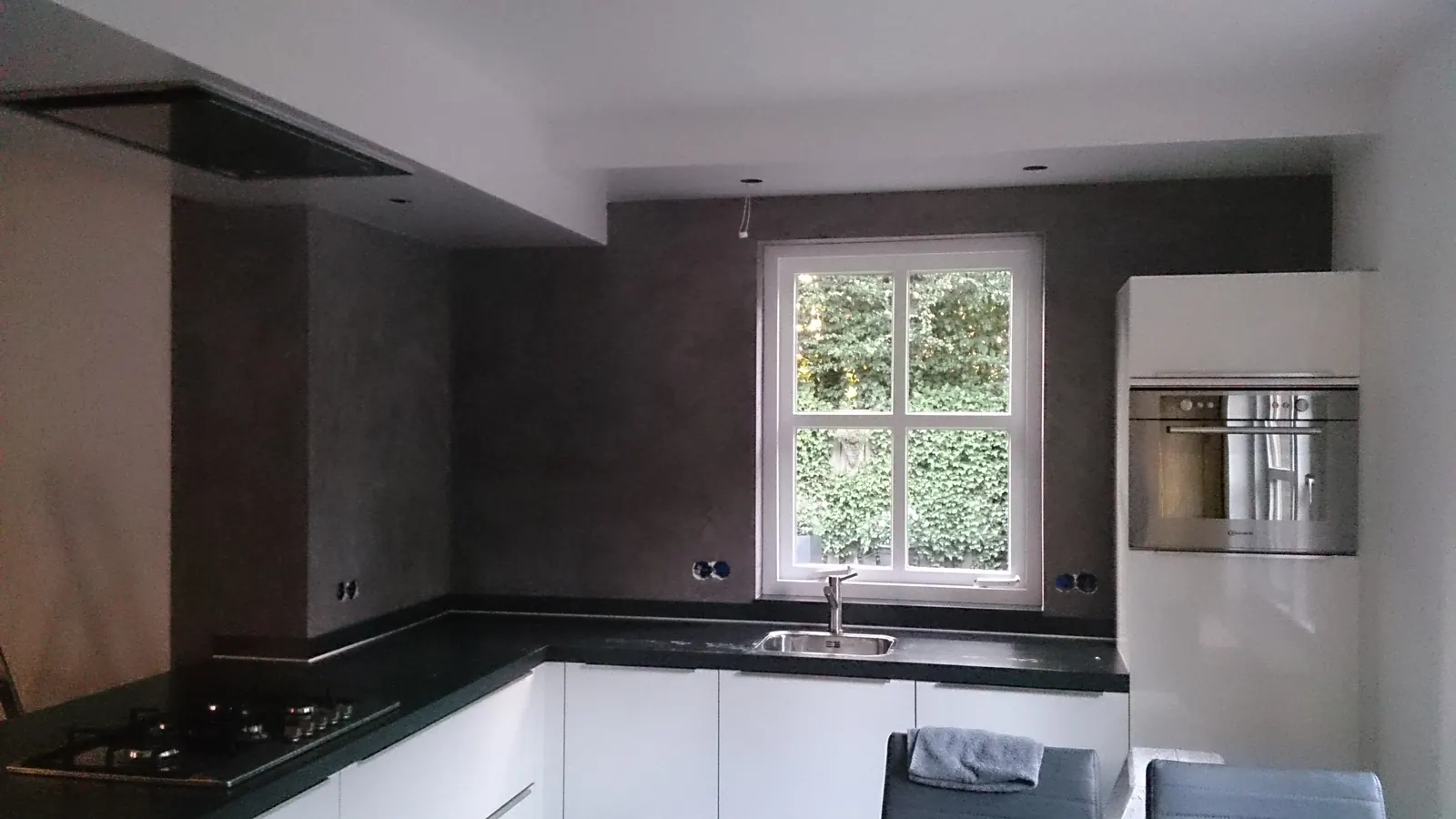 Keuken in Gemert na de aanpassing: donkere betonlook achterwand met raam en oven